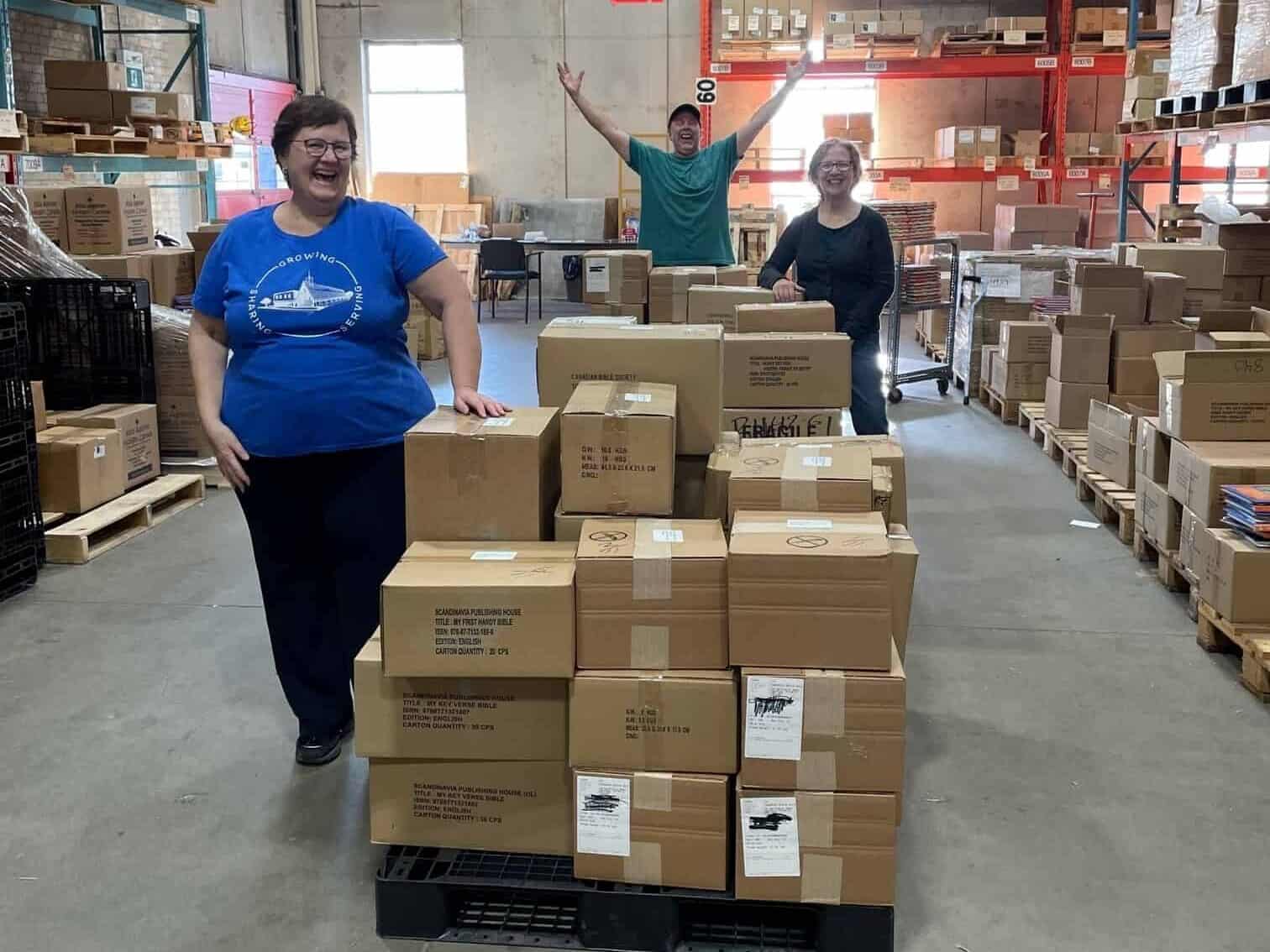 Three workers standing with a skid of boxes