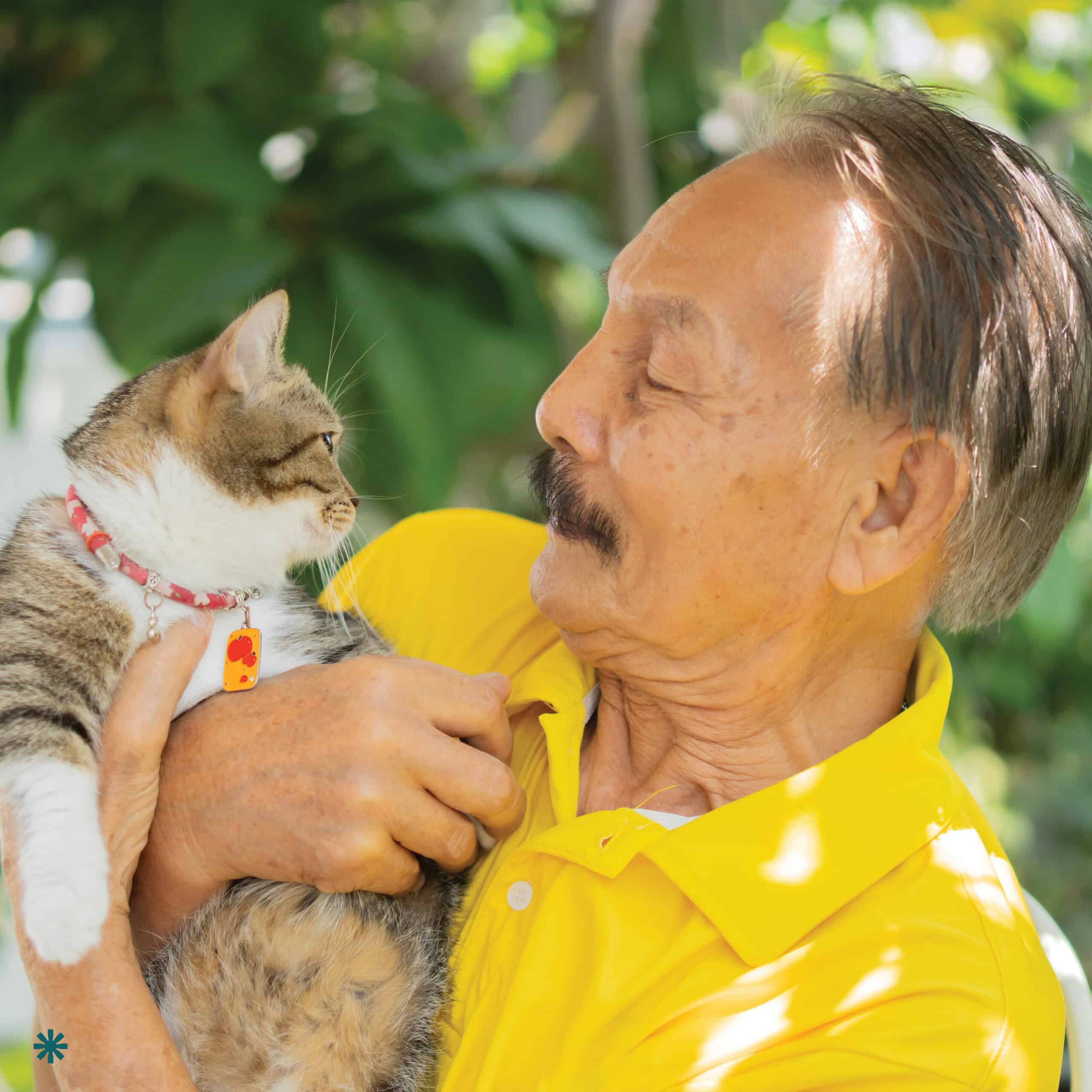 Elderly man wearing a yellow shirt carrying his cat. *Name and photo has been changed to protect privacy.