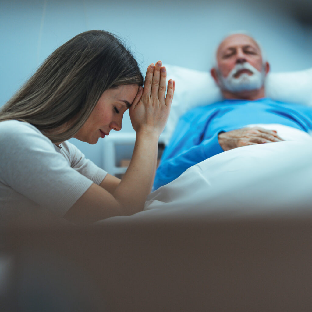 A woman praying for a sick elderly man.