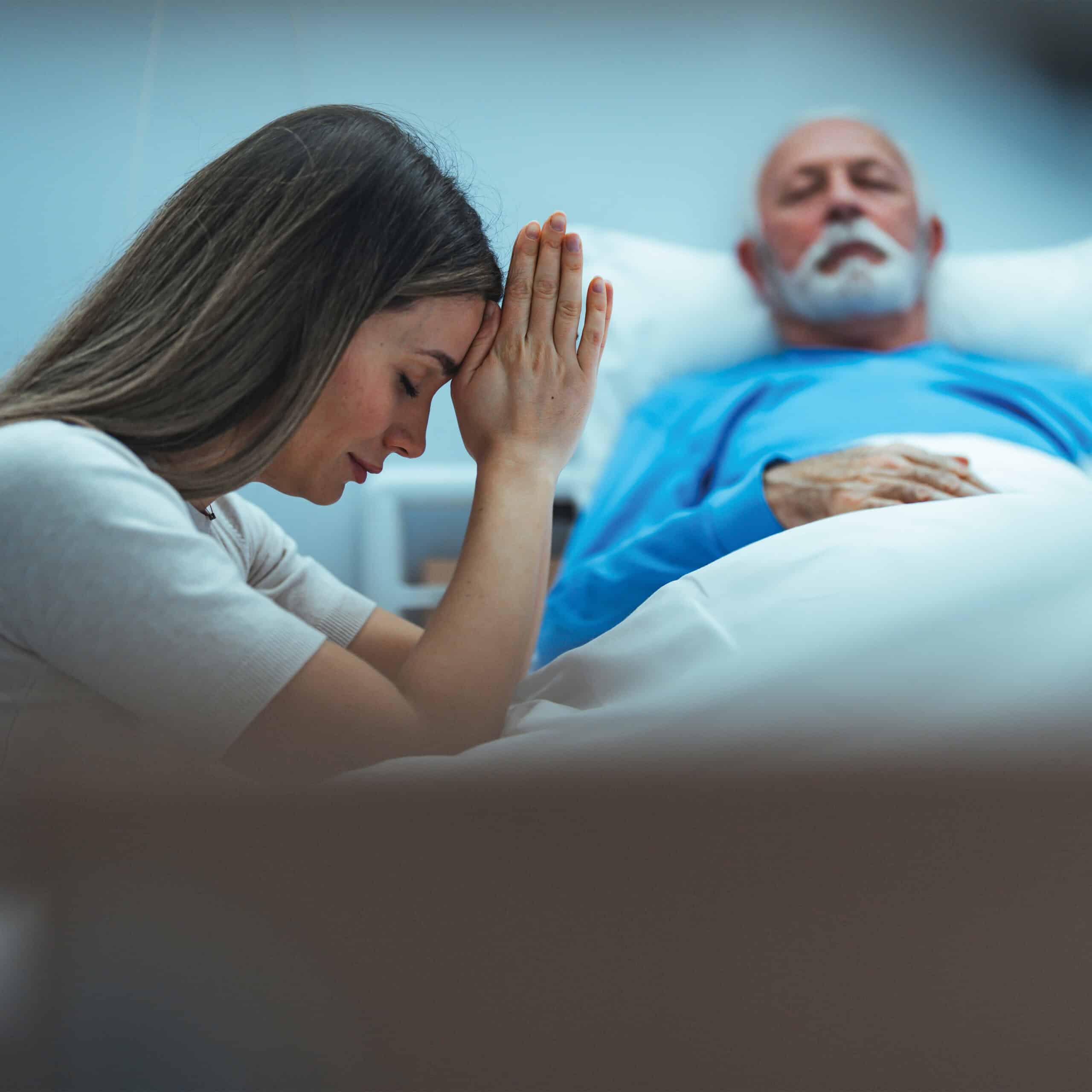 A woman praying for a sick elderly man.